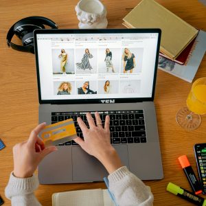 Hands holding credit card making online purchase on laptop at wooden desk with various items.